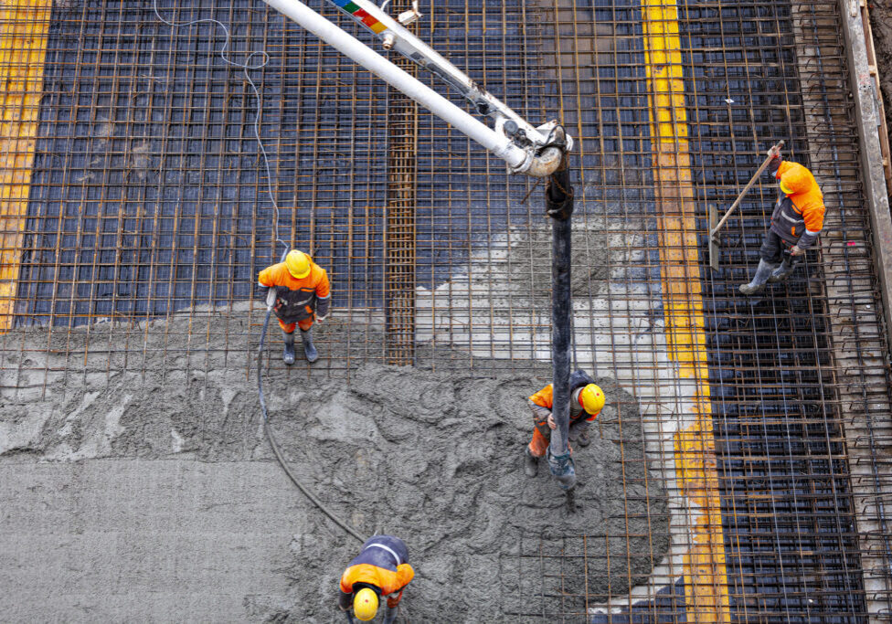 Construction workers pouring concrete on rebar